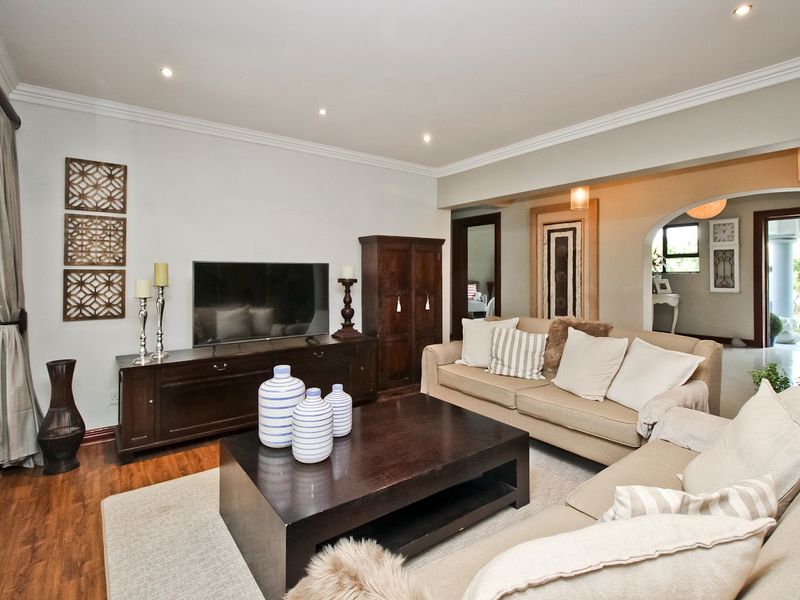 A well-maintained living room featuring hardwood flooring, recessed downlighting, crown molding, and an elegant archway leading to an adjacent space.