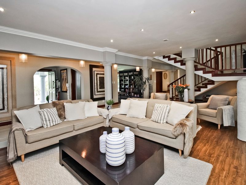 Spacious open-plan living area featuring elegant columns, an arched entryway, a wooden staircase with balustrade, and recessed lighting throughout.