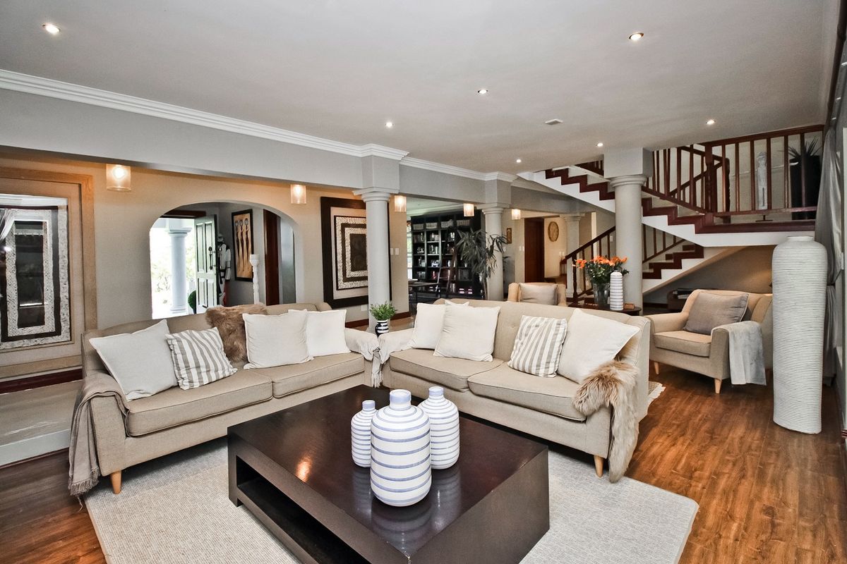 Spacious open-plan living area featuring elegant columns, an arched entryway, a wooden staircase with balustrade, and recessed lighting throughout.