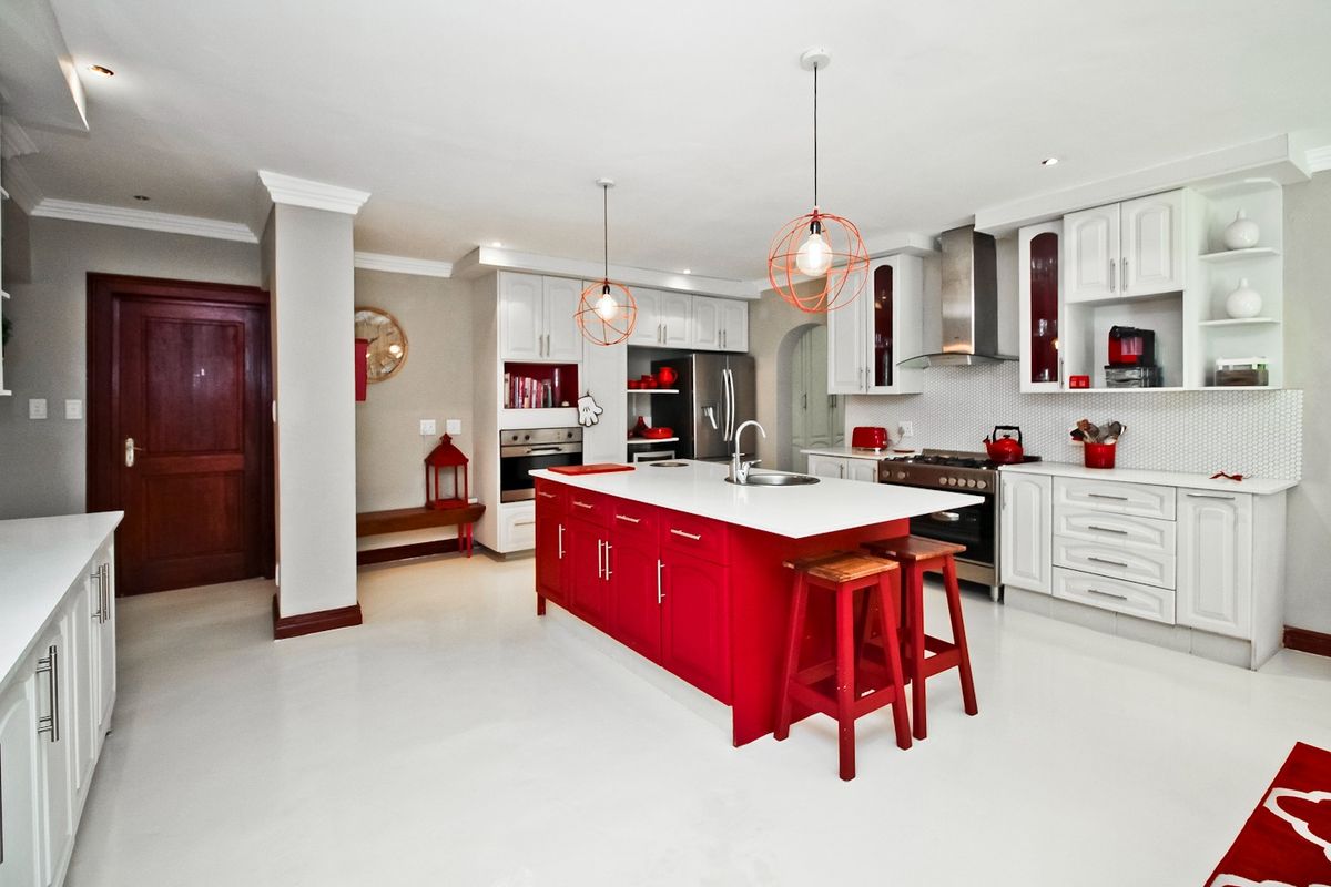 Modern kitchen featuring a vibrant red central island, white cabinetry, stone countertops, integrated appliances, and stylish pendant lighting.