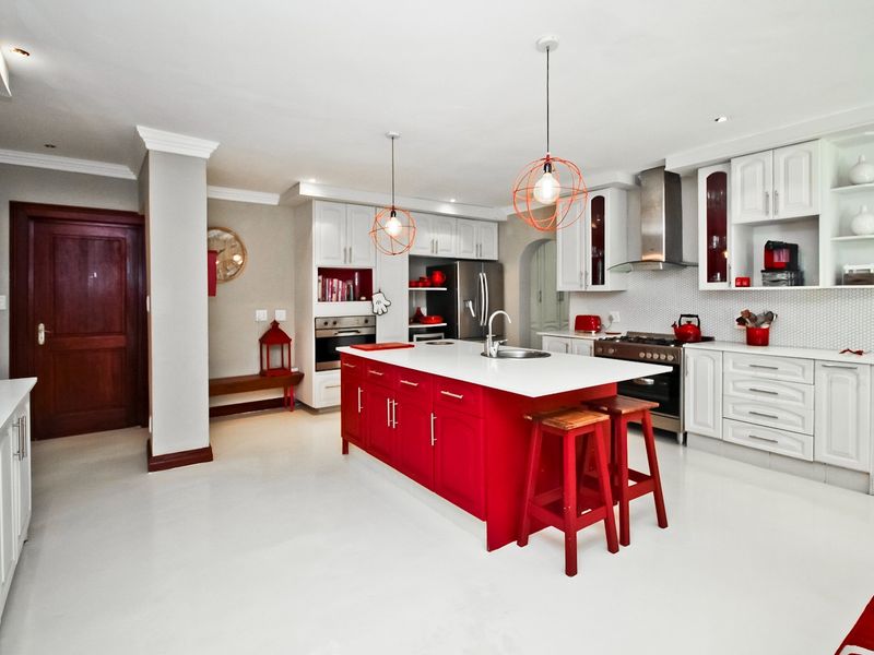 Modern kitchen featuring a vibrant red central island, white cabinetry, stone countertops, integrated appliances, and stylish pendant lighting.