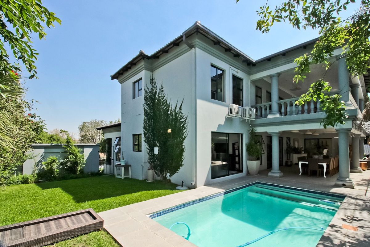 Rear view of a two-story house featuring a swimming pool, covered patio, balcony with stone columns, and well-maintained garden area.