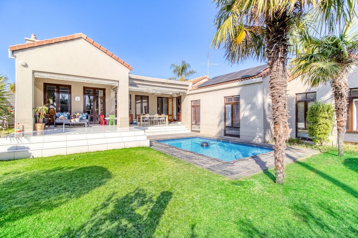 Rear view of the property featuring a tiled patio, swimming pool, and well-maintained garden area with solar panels installed on the roof.
