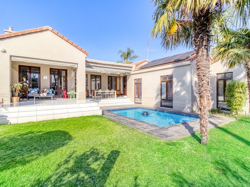 Rear view of the property featuring a tiled patio, swimming pool, and well-maintained garden area with solar panels installed on the roof.