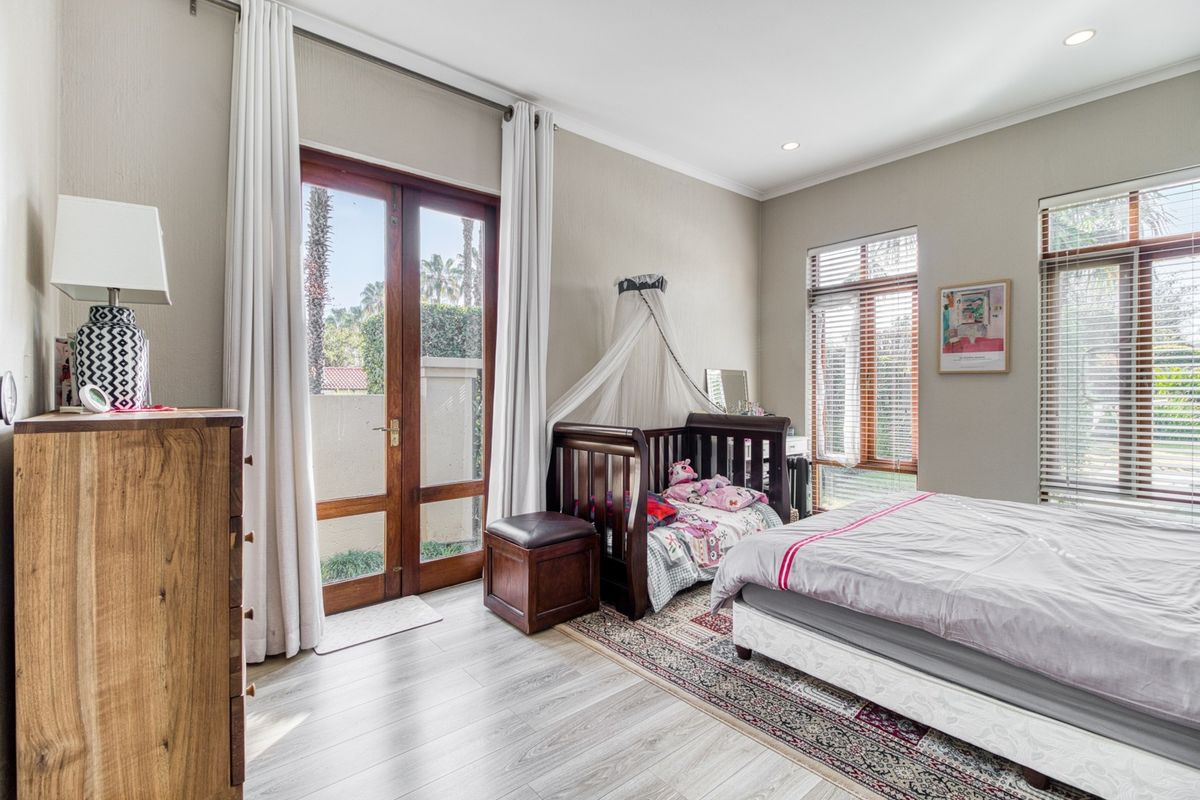 Spacious bedroom featuring laminate flooring, large windows with blinds, and a wooden glass door providing direct access to the outdoor area.
