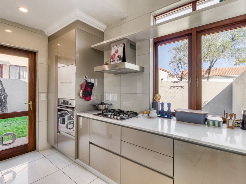 Modern kitchen featuring high-gloss cabinetry, stone countertops, a gas hob, built-in oven, and direct access to the garden through a wooden door.