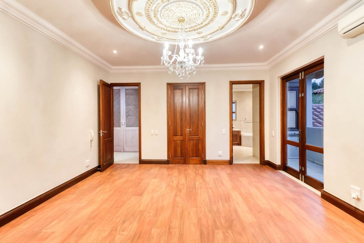 Spacious bedroom featuring wood-look flooring, ornate ceiling rose with chandelier, and direct access to an en-suite bathroom and private balcony.