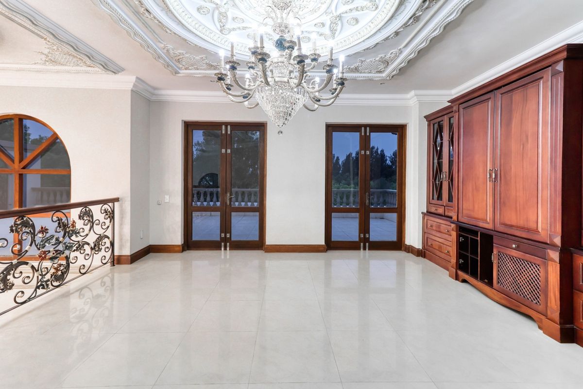 Spacious living area featuring ornate ceiling molding, a crystal chandelier, polished tile flooring, and built-in wooden cabinetry with access to a balcony.
