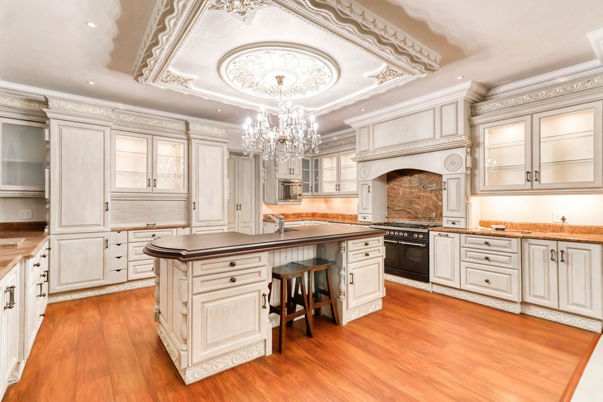 Luxurious kitchen featuring custom cabinetry, a central island with breakfast bar, ornate ceiling detailing, and high-end built-in cooking appliances.