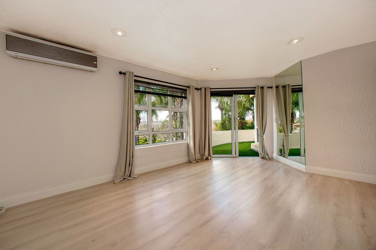 A bright, empty bedroom featuring light laminate flooring, a split-system air conditioner, recessed lighting, and sliding glass doors leading to an outdoor area.