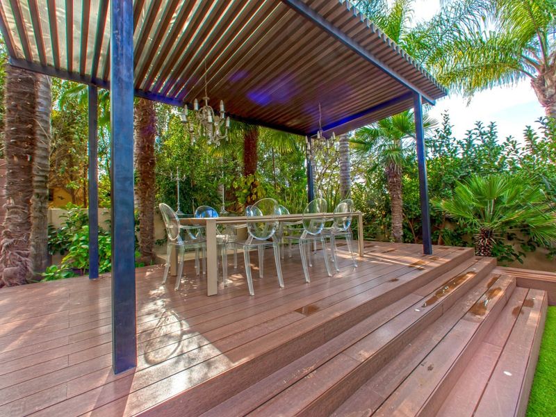 A covered outdoor patio featuring timber decking, a modern pergola structure, and stepped access to the garden area.