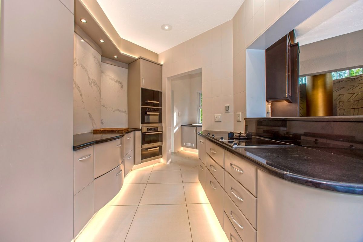 Modern kitchen featuring sleek cabinetry, built-in appliances, stone countertops, and ambient under-cabinet lighting, creating a clean and functional culinary space.