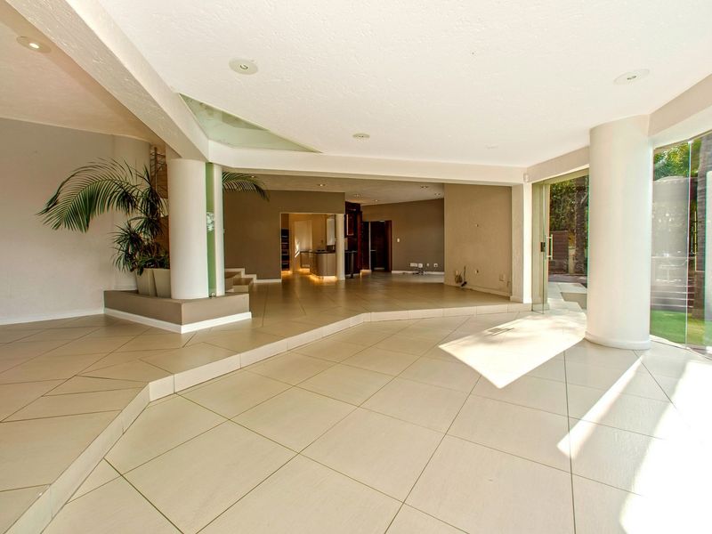 Spacious open-plan living area featuring large format floor tiles, structural columns, and expansive sliding glass doors providing seamless access to the garden.