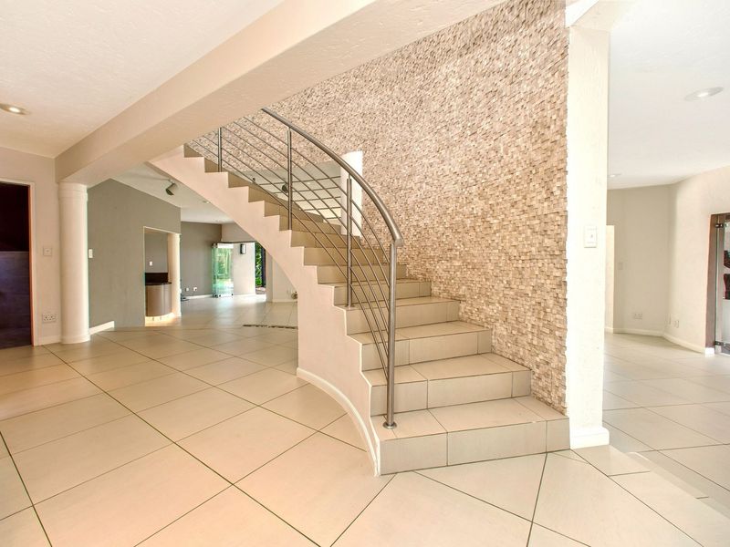 Spacious entrance hall featuring a curved tiled staircase with a modern stainless steel balustrade and a decorative stone-clad feature wall.
