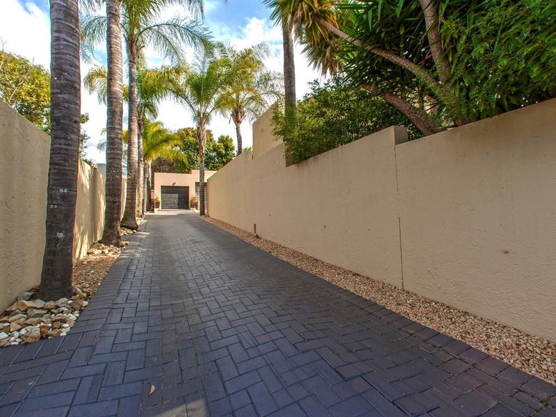 A private paved driveway leading to a garage, flanked by high boundary walls and mature palm trees.