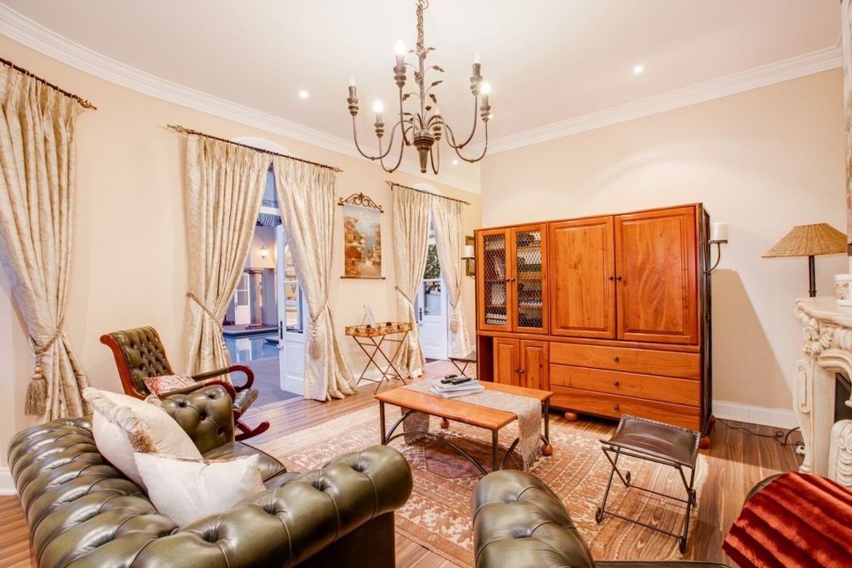 A spacious living room featuring a classic chandelier, crown molding, and a fireplace mantel, with double doors opening to an outdoor area.