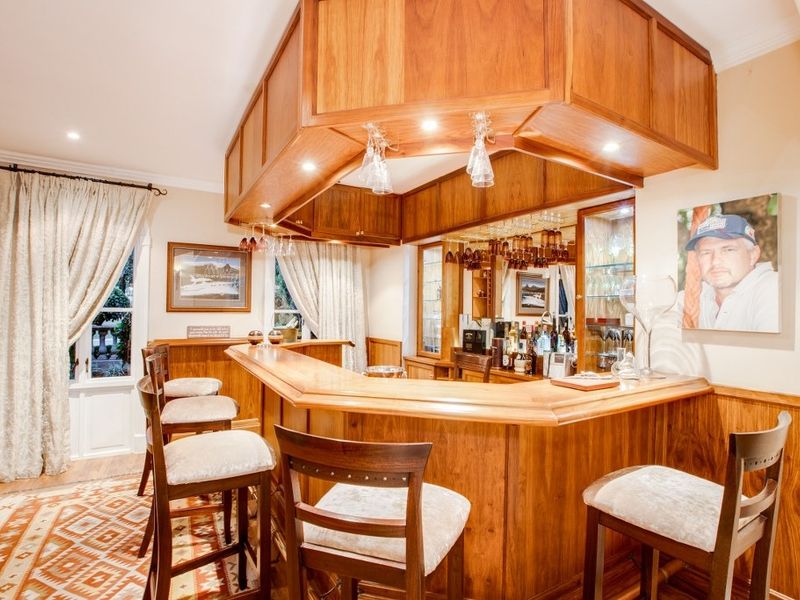 A well-appointed home bar featuring custom built-in wooden cabinetry, an overhead canopy with integrated lighting, and elegant wood paneling throughout.