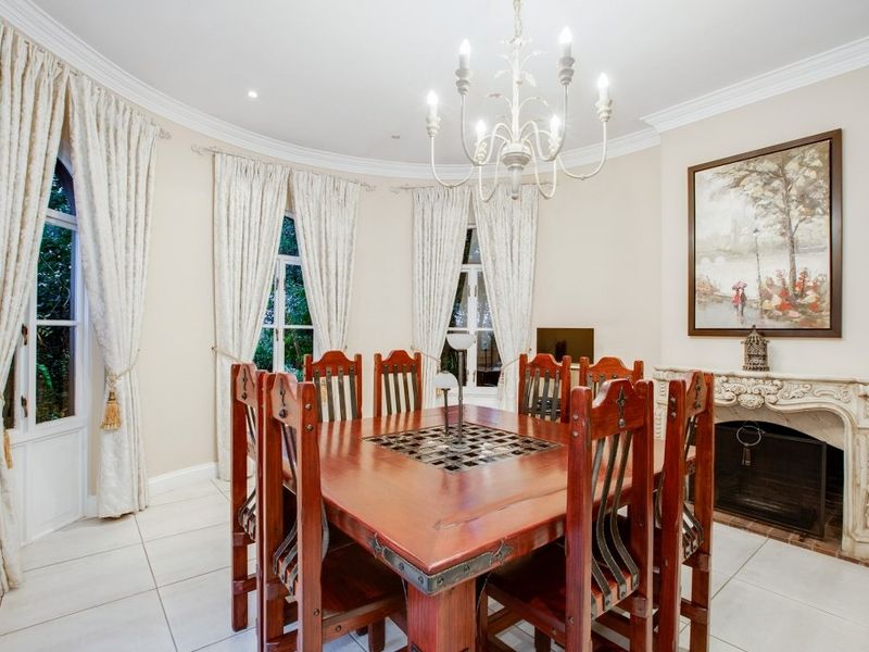 Elegant dining room featuring an ornate fireplace mantel, tiled flooring, arched windows, and classic crown molding, creating a sophisticated atmosphere for formal meals.