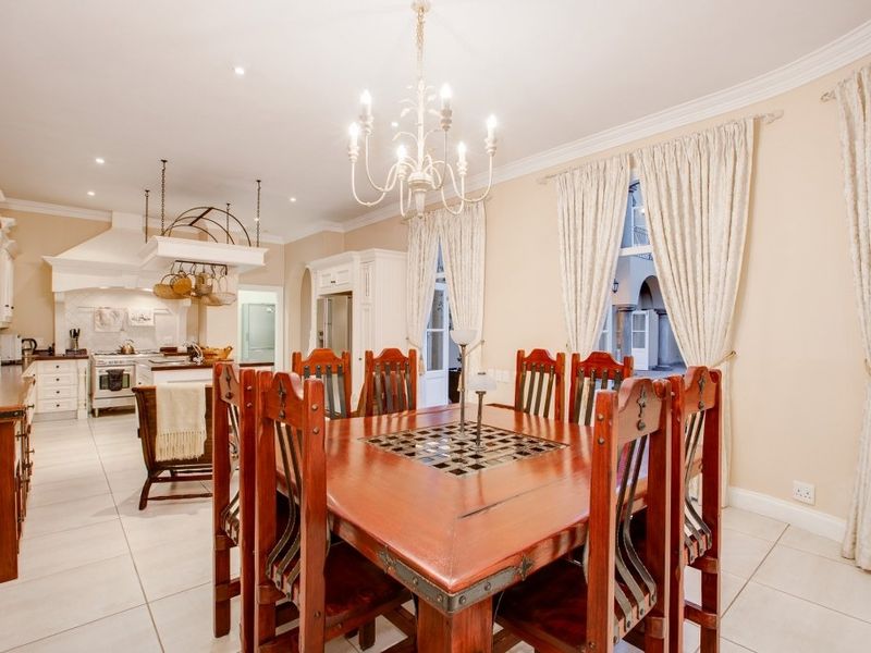 Spacious open-plan dining and kitchen area featuring tiled floors, classic cabinetry, a central chandelier, and direct access to an outdoor patio.