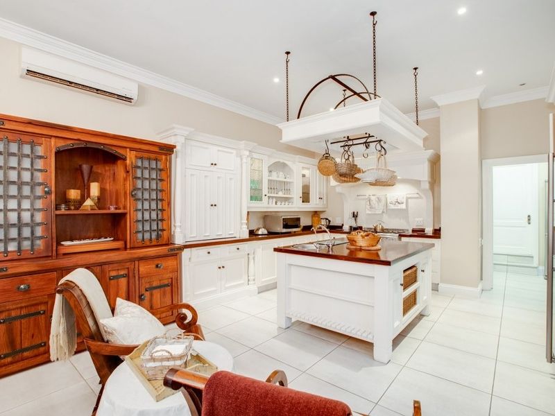 Spacious kitchen featuring a central island, custom white cabinetry, a decorative hanging pot rack, and tiled flooring with integrated air conditioning.