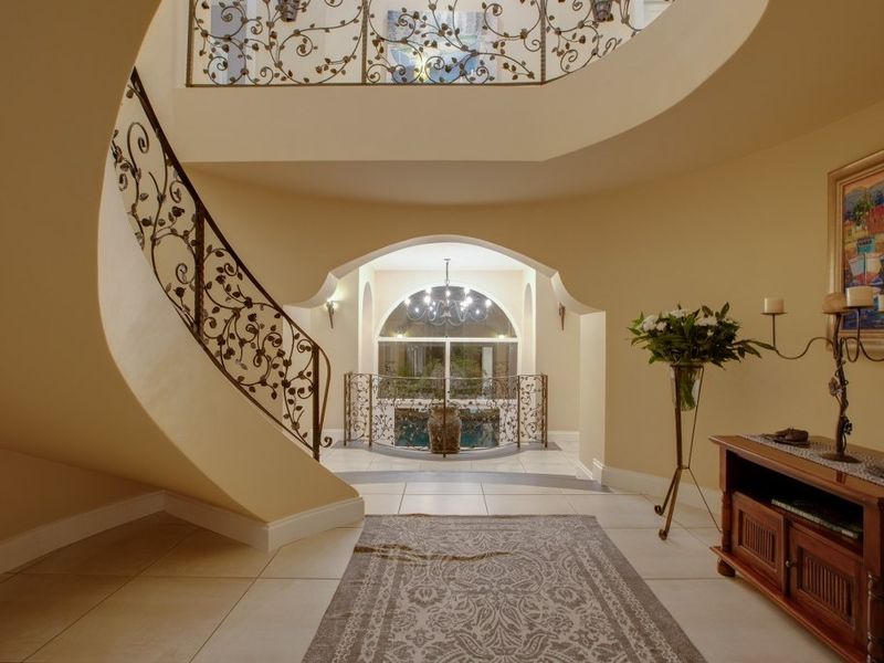 Grand entrance foyer featuring a sweeping curved staircase with ornate wrought iron balustrades, tiled flooring, and an elegant arched window overlooking the exterior.