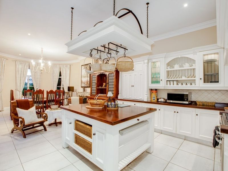 Spacious open-plan kitchen and dining area featuring a central island with a hanging pot rack, custom white cabinetry, and tiled flooring.