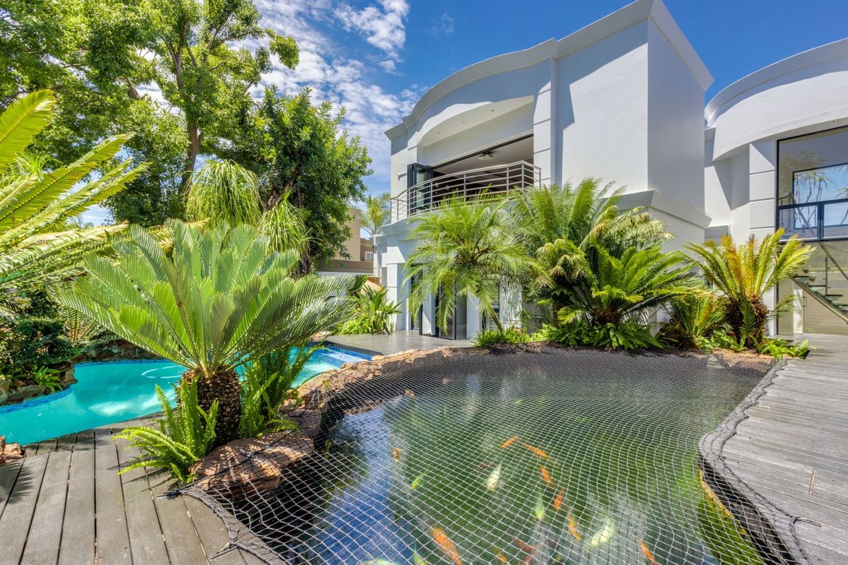 A beautifully landscaped rear garden featuring a swimming pool, a koi pond with safety netting, and timber decking leading to a modern two-story residence.