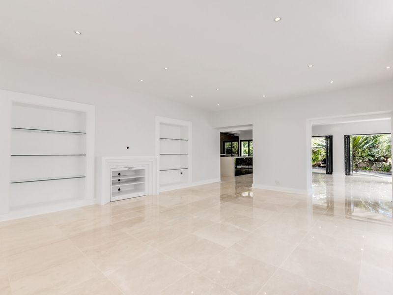 Spacious, light-filled living area featuring polished marble flooring, recessed downlighting, and custom built-in shelving units with glass inserts.