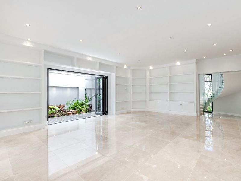 Spacious living area featuring extensive built-in shelving, polished marble flooring, recessed lighting, and seamless access to a private courtyard through bi-fold doors.