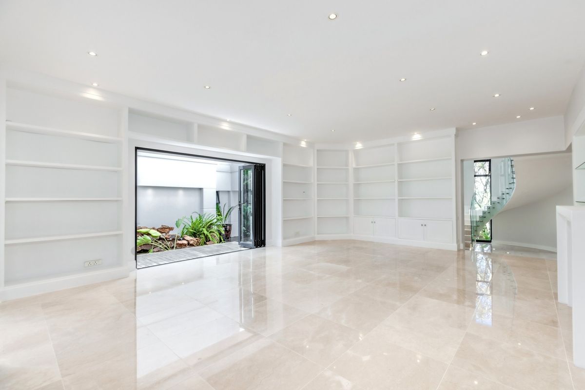 Spacious living area featuring extensive built-in shelving, polished marble flooring, recessed lighting, and seamless access to a private courtyard through bi-fold doors.