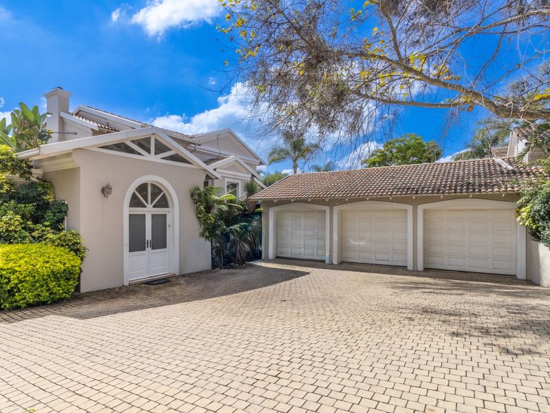 Front elevation of a well-maintained house featuring a triple garage, paved driveway, and an elegant arched entrance.