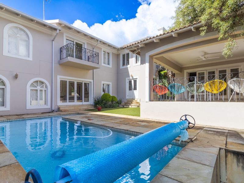 A well-maintained rear exterior featuring a swimming pool with stone decking, a covered patio area, and a balcony with decorative wrought iron railings.