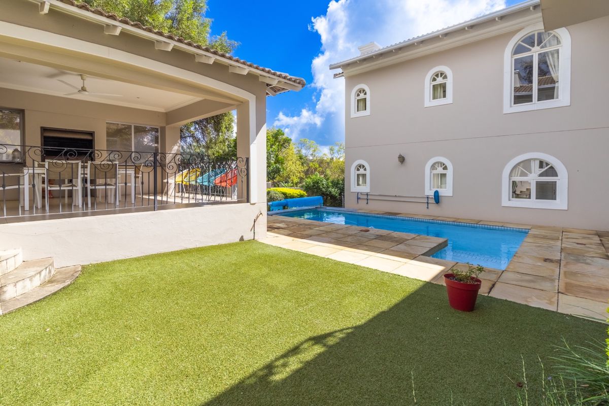 Rear exterior view featuring a swimming pool, covered patio area with wrought iron railing, and well-maintained artificial lawn.