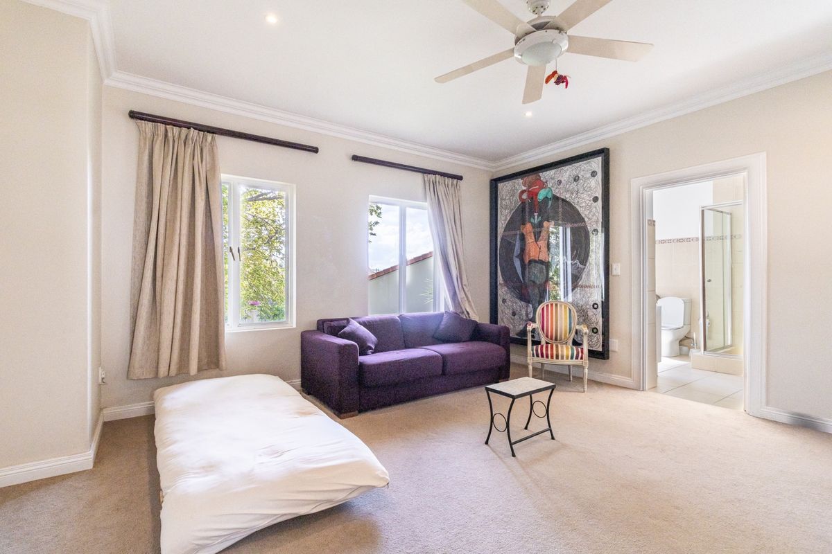 Spacious bedroom featuring neutral carpeting, crown molding, a ceiling fan, and an attached en-suite bathroom with a shower.