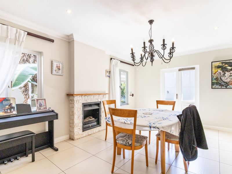 Bright dining room featuring tiled flooring, a stone-clad fireplace, and a classic wrought iron chandelier, with direct access to the outdoor area via french doors.