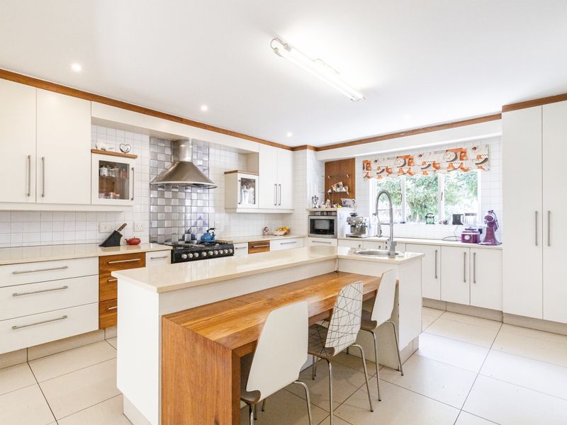 A well-appointed kitchen featuring white cabinetry, stone countertops, a gas hob with stainless steel splashback, and a central island with integrated breakfast bar seating.