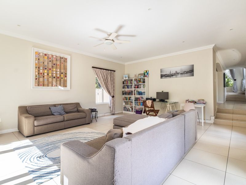 Spacious living room featuring neutral tiled flooring, recessed lighting, and a ceiling fan, with an open transition to the adjacent staircase area.