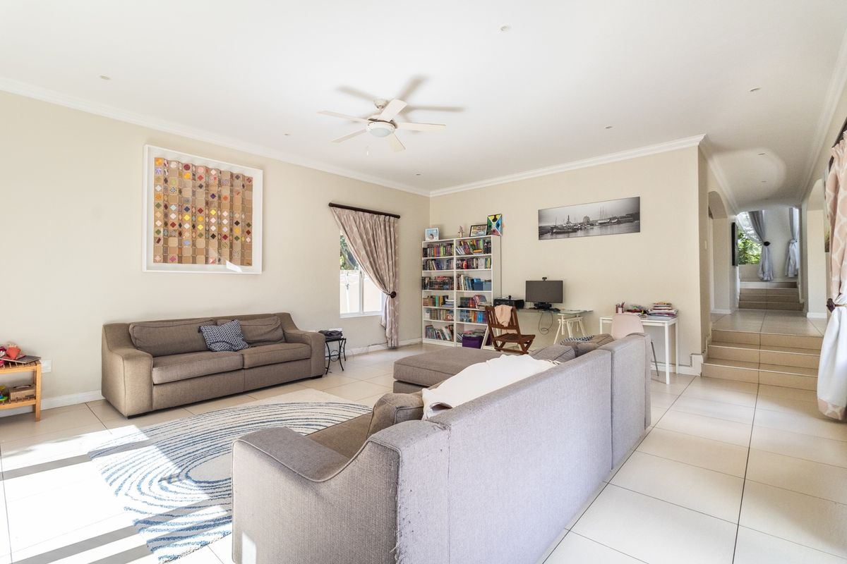 Spacious living room featuring neutral tiled flooring, recessed lighting, and a ceiling fan, with an open transition to the adjacent staircase area.