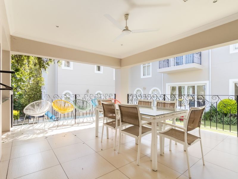 Spacious covered patio featuring tiled flooring, a built-in braai, ceiling fan, and decorative wrought iron balustrade overlooking the garden area.