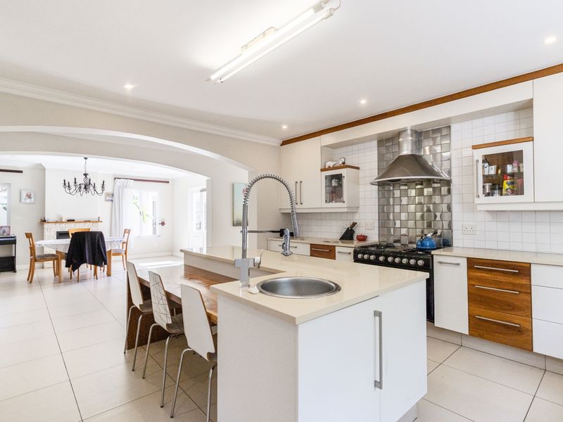 Spacious open-plan kitchen featuring a central island with sink, gas cooktop, modern cabinetry, and tiled flooring, flowing into an adjacent dining area.