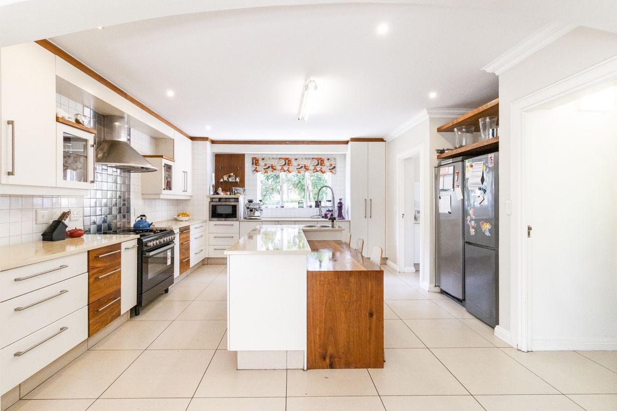 Spacious modern kitchen featuring a central island with wooden breakfast bar, stone countertops, gas stove, and ample built-in cabinetry with tiled flooring.
