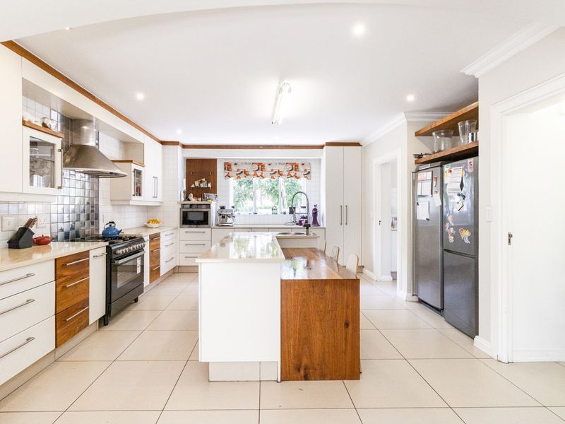 Spacious modern kitchen featuring a central island with wooden breakfast bar, stone countertops, gas stove, and ample built-in cabinetry with tiled flooring.