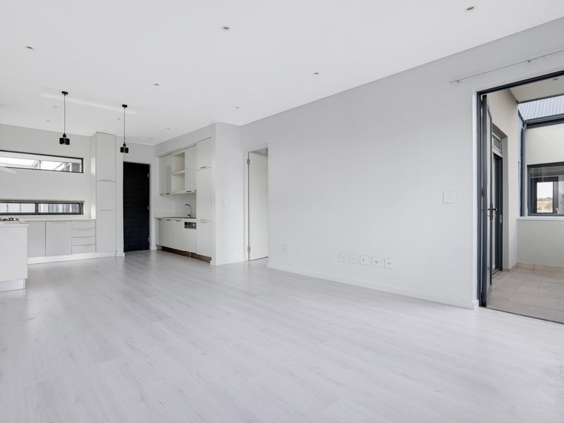 Modern open-plan living area featuring a sleek kitchen with built-in cabinetry, hob, and extractor fan, leading to an outdoor balcony space.