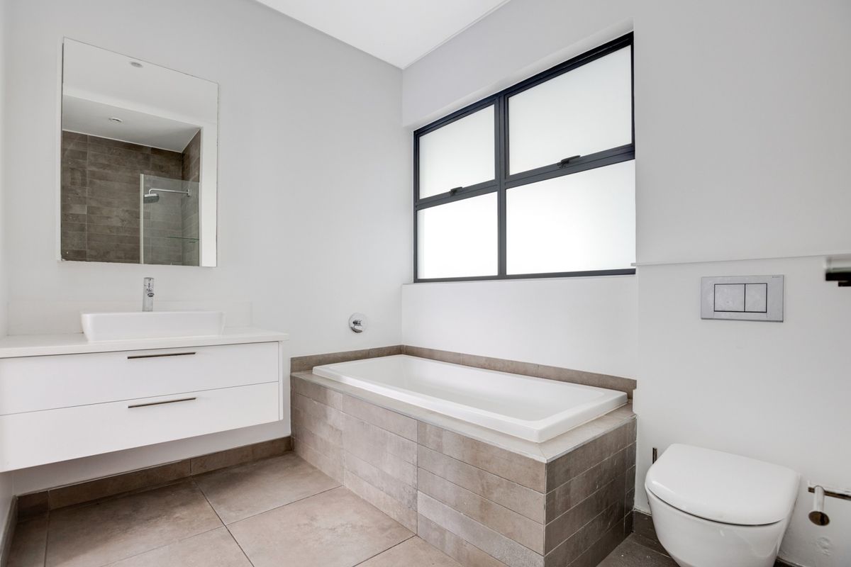 Modern bathroom featuring a floating vanity with vessel sink, wall-hung toilet, and a tiled built-in bathtub with neutral finishes.