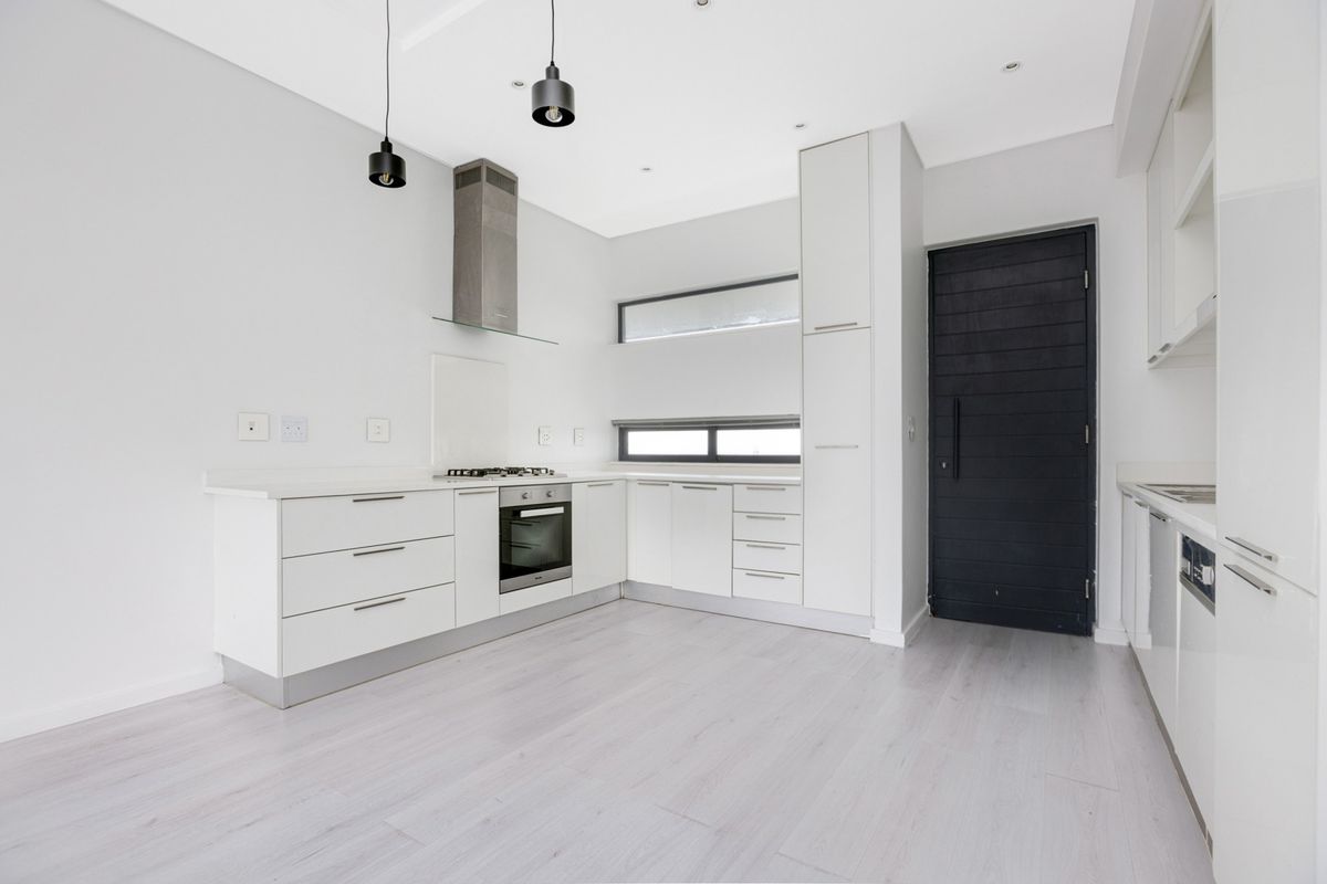 Modern, minimalist kitchen featuring white cabinetry, stone countertops, integrated appliances, and sleek pendant lighting in a bright, open-plan layout.