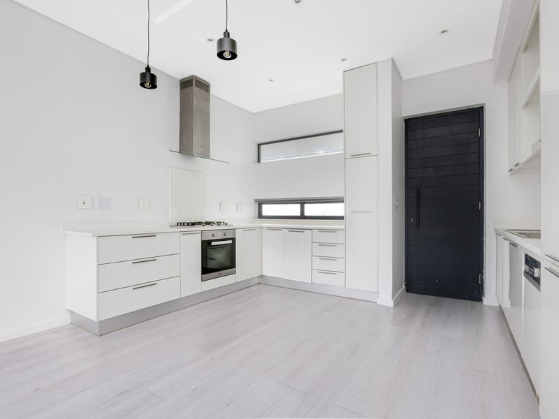Modern, minimalist kitchen featuring white cabinetry, stone countertops, integrated appliances, and sleek pendant lighting in a bright, open-plan layout.