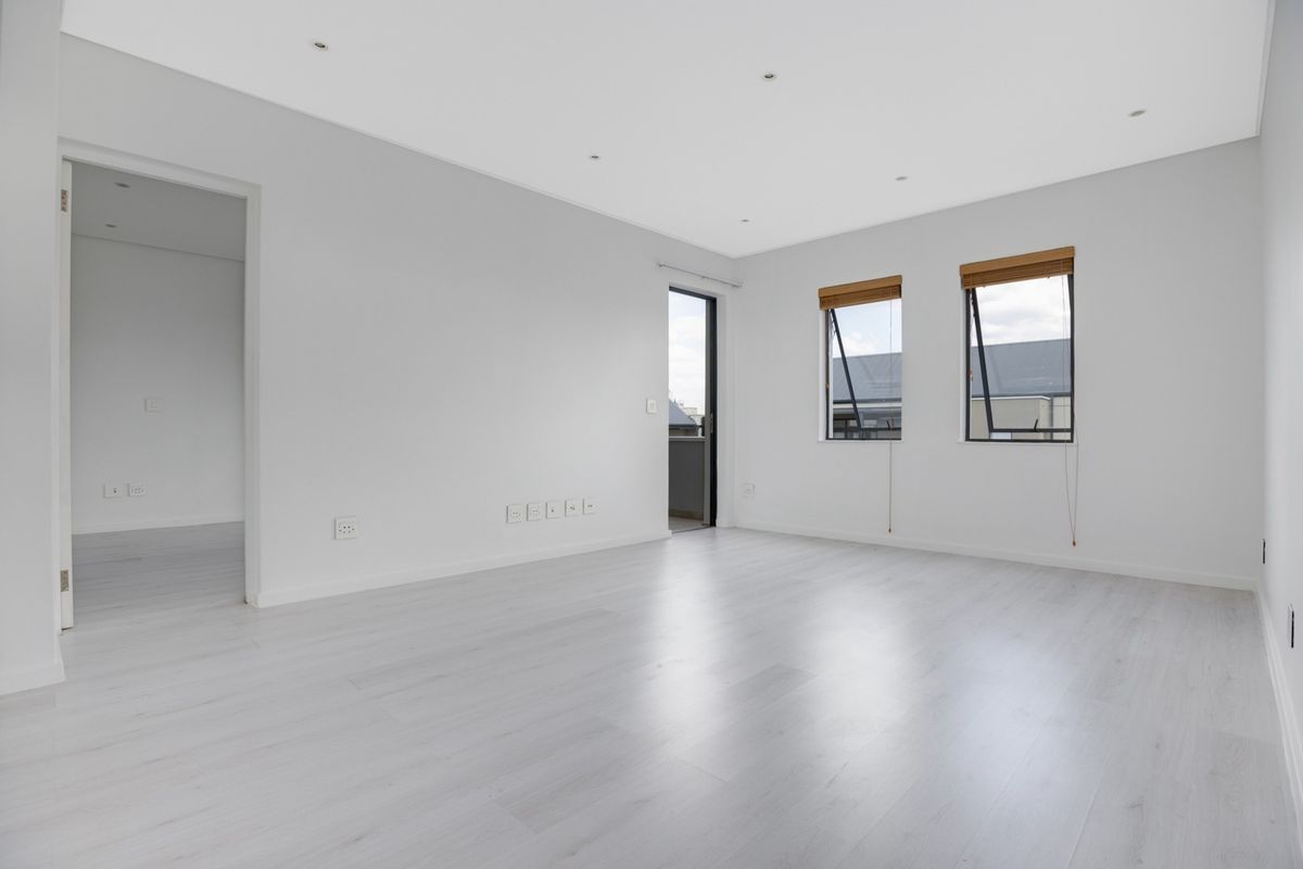 A bright, empty living room featuring modern laminate flooring, recessed downlights, and direct access to a balcony through a glass door.