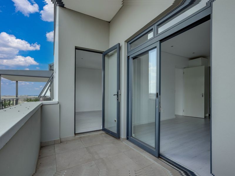 A modern balcony featuring tiled flooring, aluminium sliding doors, and a parapet wall, offering a seamless transition to the interior living space.