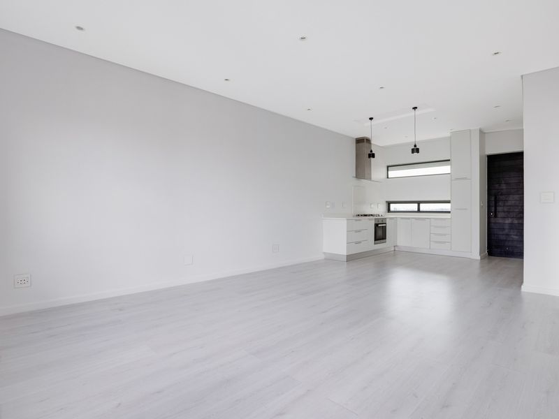A bright, modern open-plan living and kitchen area featuring sleek white cabinetry, integrated appliances, and light-toned laminate flooring throughout.