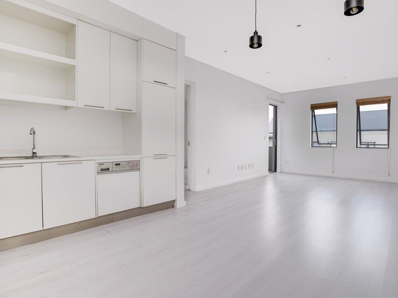 Bright open-plan living area featuring modern white cabinetry, integrated dishwasher, laminate flooring, and large windows providing ample natural light.